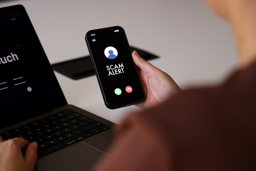 A hand holding a phone showing an incoming call labeled scam alert